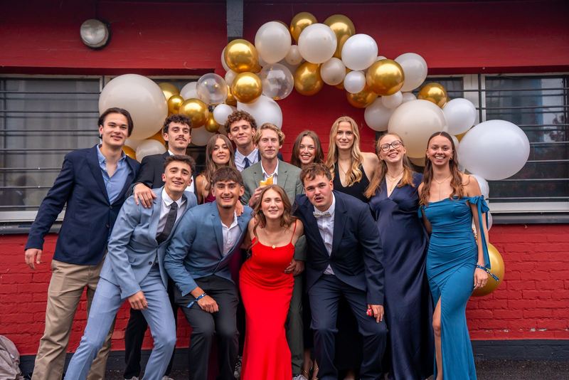 Bal de la promo 2029 — photo de groupe devant une façade rouge sous une arche de ballons dorés